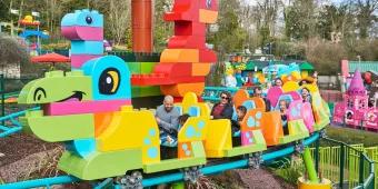 Adults and young children riding a rollercoaster designed to look like a dinosaur made with colourful DUPLO bricks