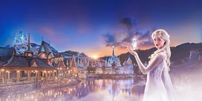 the Disney Princess Elsa standing before the illuminated World of Frozen land, depicting the village of Arendelle and the Ice Palace, coming soon to Disneyland Paris.