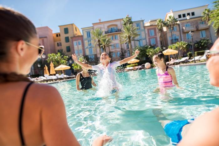 Group of kids splashing around in a pool surrounded by palm trees