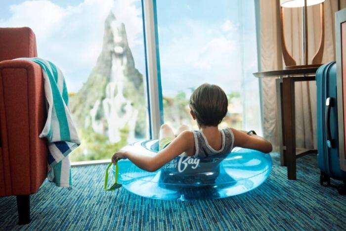 Little kid sitting in a swim ring in a hotel room with a view of Volcano Bay Water Park