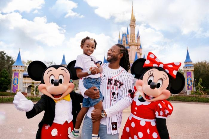 Smiling dad holding his child next to Mickey and Minnie in front of Cinderella castle