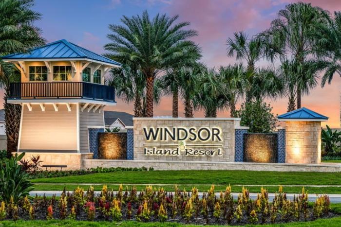 A stone and tile entrance sign for Windsor Island Resort at sunset, flanked by a tall guard tower structure, palm trees, and colourful flowers in the foreground.