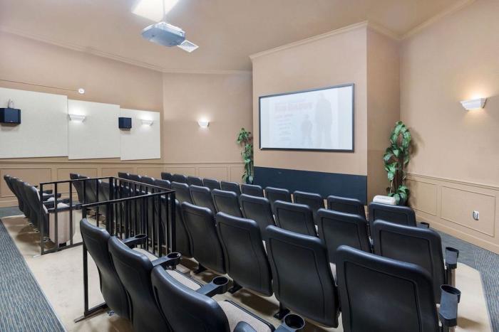An indoor resort movie theater with rows of black leather stadium seats facing a large projection screen.
