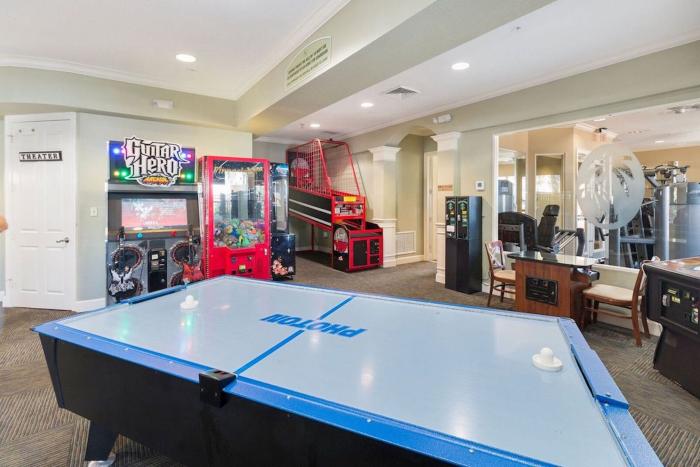 An indoor resort game room with an air hockey table, basketball arcade game, and Guitar Hero cabinet.
