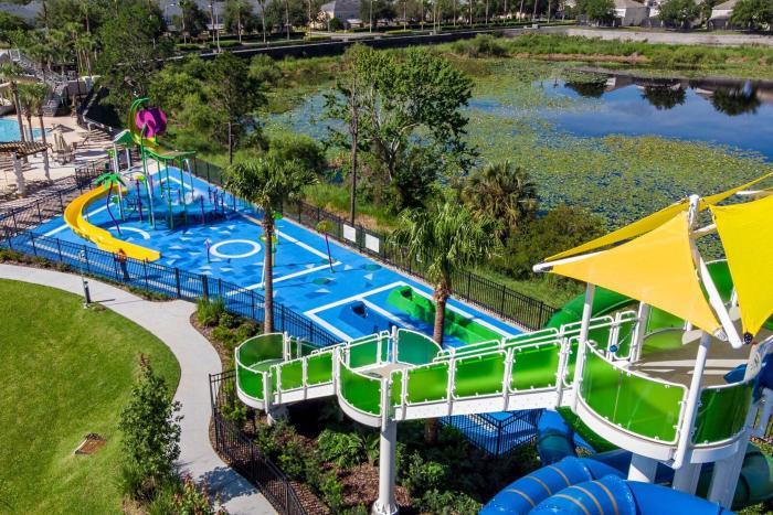 Aerial view of a resort water park with a blue splash pad, large green and blue water slides, and a lily pad lake in the background.