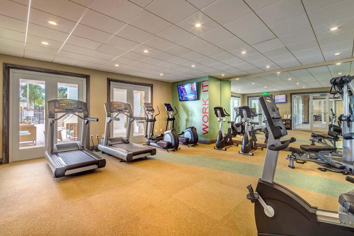 An indoor resort gym featuring treadmills, ellipticals, stationary bikes, free weights, and a wall mirror under a tiled ceiling.