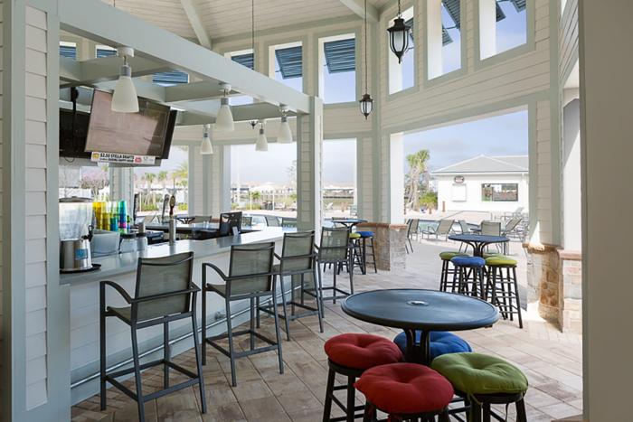 Bright, open-air resort bar area with bar stools, tables, and colorful cushions