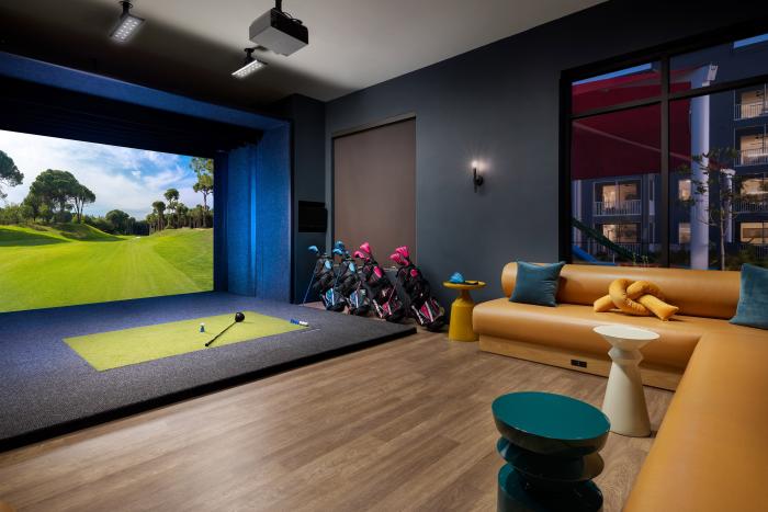 Luxury indoor golf simulator lounge with a large screen, golf clubs, and a leather sectional sofa