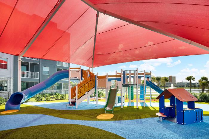 Children's outdoor playground with slides and climbing structures under a large red sun shade sail