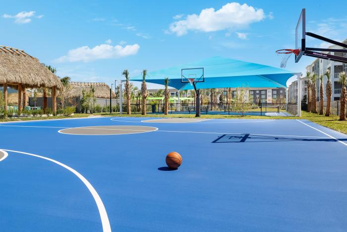 Professional blue outdoor basketball court with a basketball in the foreground and a blue shade canopy