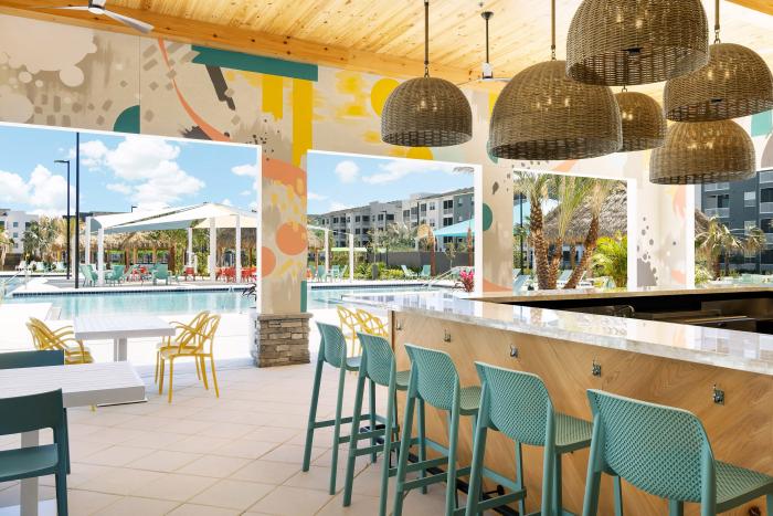 Poolside restaurant bar with woven wicker pendant lights, teal barstools, and colorful murals facing the pool