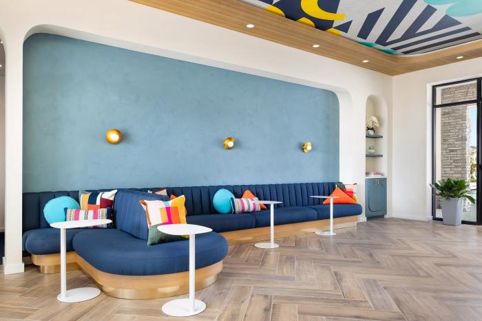 Modern lobby seating area with a long blue velvet sofa, colorful geometric pillows, and a blue accent wall