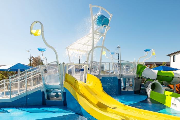 Children's water splash playground with a dumping bucket and yellow water slide under a blue sky