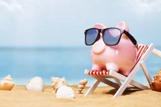 A pink piggy bank wearing sunglasses and sitting on a deck chair on a beach