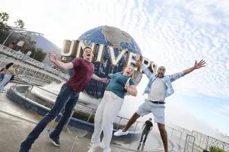 Three people jumping excitedly in front of the Universal Globe