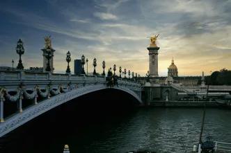 A bridge over the river seine with the sunsetting in the background. there are golden statues on the bridge.
