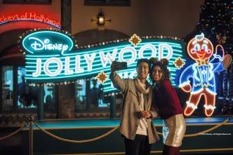 A couple taking a selfie in front of a neon sign for Disney Jollywood Nights