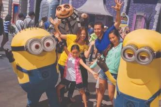A joyful family with two young kids raising their hands in excitement while meeting the Minions and Gru at Universal Studios Florida, highlighting an essential Universal Orlando Resort experience.