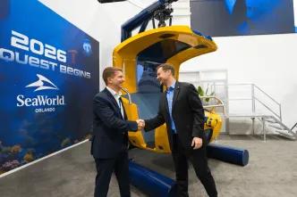 Two men shaking hands in front of the ride vehicle, a yellow hanging seat.