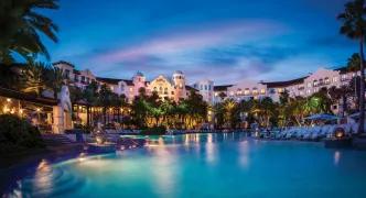 Illuminated lagoon-style swimming pool and tropical architecture at a premium Universal Orlando Resort hotel at night.