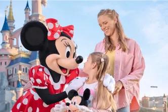 A young girl and her mother smiling with the Minnie Mouse character in front of Sleeping Beauty Castle at Disneyland Paris.