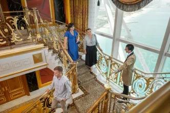Guests on the Burj Al Arab Inside Tour walking down the luxurious gold staircase with an attendant, showcasing the opulent interior and expansive ocean view.