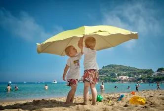 Children playing with beach umbrella on family summer vacation.