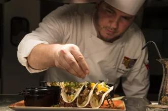 A chef garnishing fresh gourmet tacos on a platter at a Universal Orlando Resort restaurant.