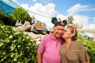 Couple wearing Mickey and Minnie ears near The Seas with Nemo & Friends pavilion at EPCOT, with Spaceship Earth in the background