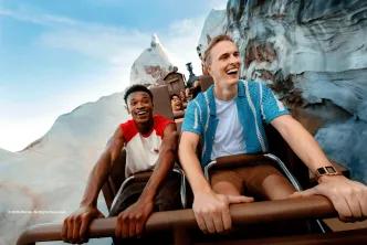 Two young men laughing as they ride the Expedition Everest roller coaster train through snow-covered mountain peaks