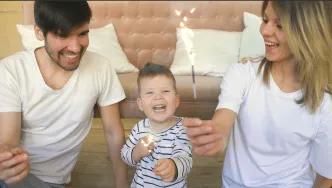 A young family celebrating together at home with sparklers, smiling and laughing