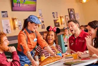 Server presenting food to a laughing group of guests at the Sports Bar & Lounge presented by Coca-Cola, Disney Village
