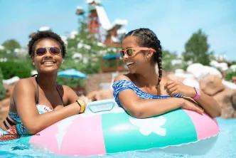 Two smiling women floating together on a colorful inflatable inner tube in a water park pool