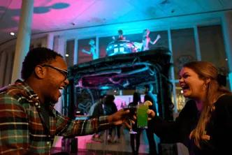 Two guests laughing and clinking colorful themed cocktails at a Universal Orlando Resort hotel Halloween Horror Nights bar experience