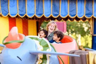 A smiling woman and two young boys riding the Dumbo the Flying Elephant attraction
