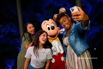 Two guests taking a selfie with Mickey Mouse at night