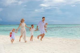 A family dressed in white holding hands and running along a tropical white-sand beach