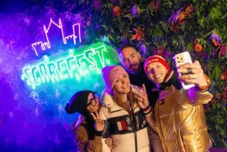 Four friends taking a selfie in front of a glowing neon Scarefest sign