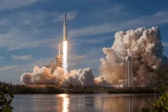 A SpaceX Falcon Heavy rocket launching from the pad, surrounded by large plumes of exhaust
