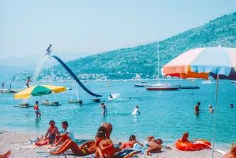 Sunbathers and swimmers enjoying a busy Mediterranean beach with a water slide and parasols.