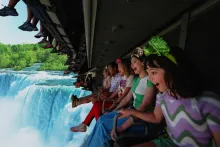 A row of people on a ride vehicle hanging a screen showing a waterfall