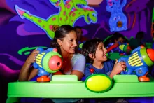A mother and sun in a neon green ride vehicle using plastic laser blasters to shoot targets