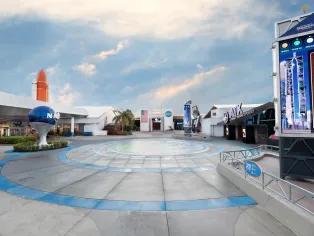 Kennedy Space Center A paved plaza surrounded by space themed buildings, with a large model of the NASA logo to the left-hand side