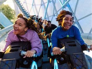 Guests riding TRON Lightcycle/Run Two guests smiling as they are launched, sat on bike shaped vehicle riding TRON Lightcycle/Run
