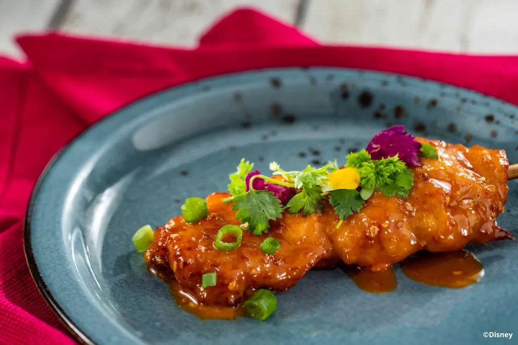 Spicy Mala Chicken Skewer at Lotus House Chicken skewer on a plate topped with sauce, spring onions and herbs