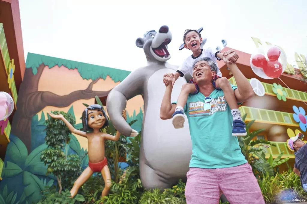 Disney's Pop Century Resort A man carrying a young boy on his shoulders standing in front of a large sculpture of Baloo and Mowgli