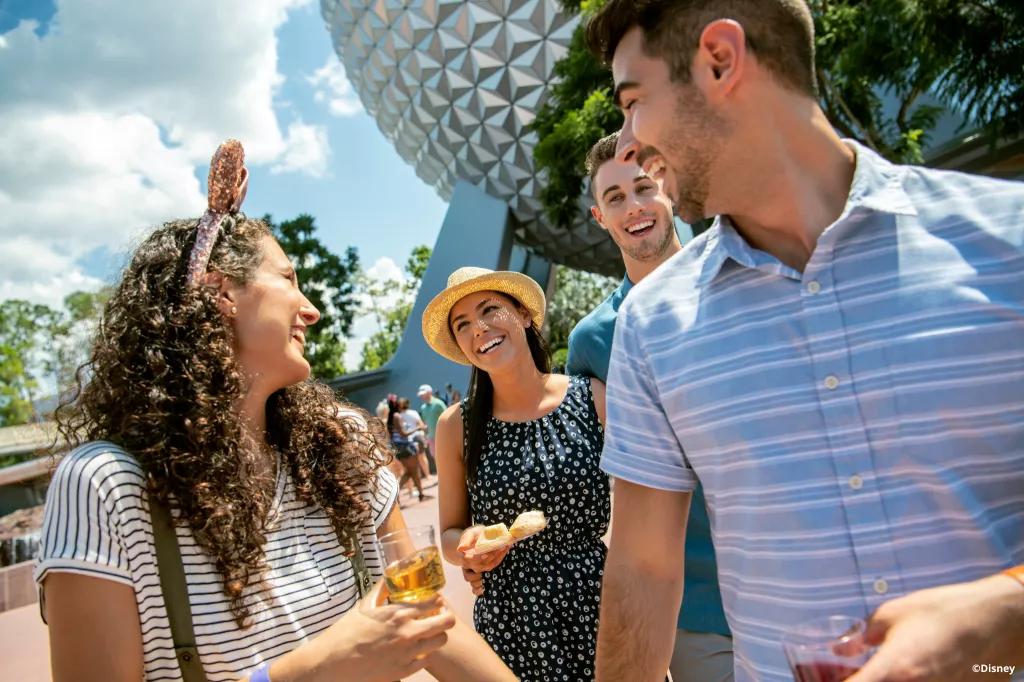 EPCOT Food and Wine Festival Four guests walking and talking to each other in front of Spaceship earth while eating and drinking