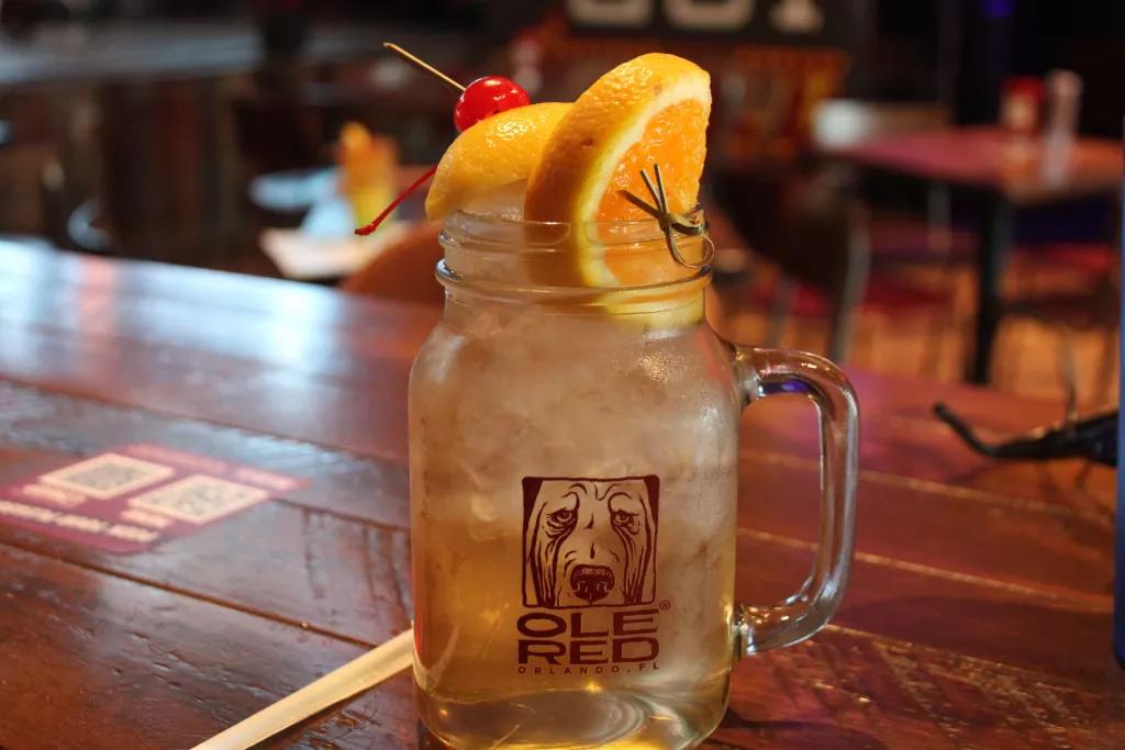 Ole Red White Sangria A mason jar glass of white sangria on a wooden bar topped with orange slices