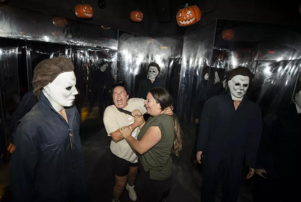 Halloween Haunted House Two women surrounded by multiple scare actors dressed as Michael Myers from Halloween