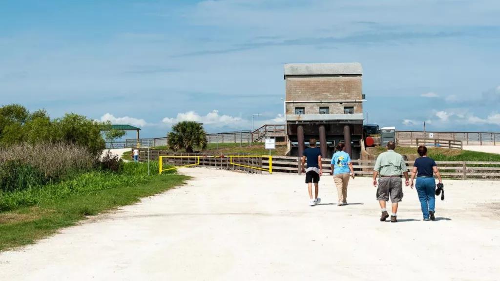 Visitors at Lake Apopka Wildlife Drive 4 adults walking along a sandy road towards a hut and the water of Lake Apopka